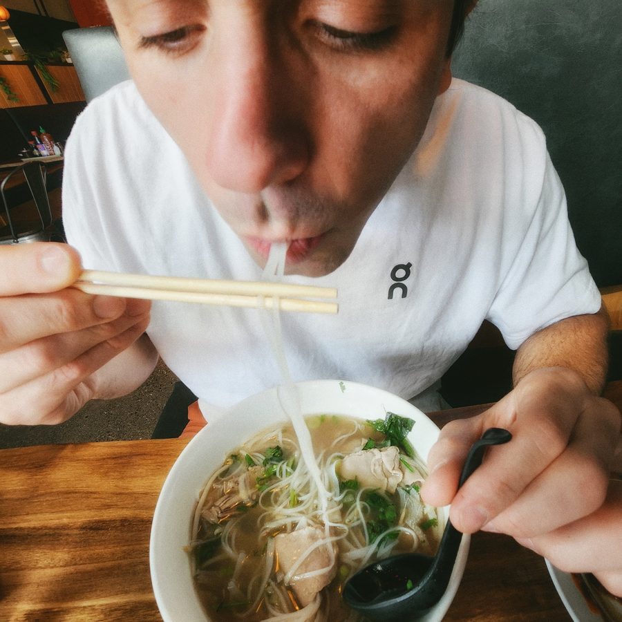 Sam Inden eating a bowl of pho with chopsticks