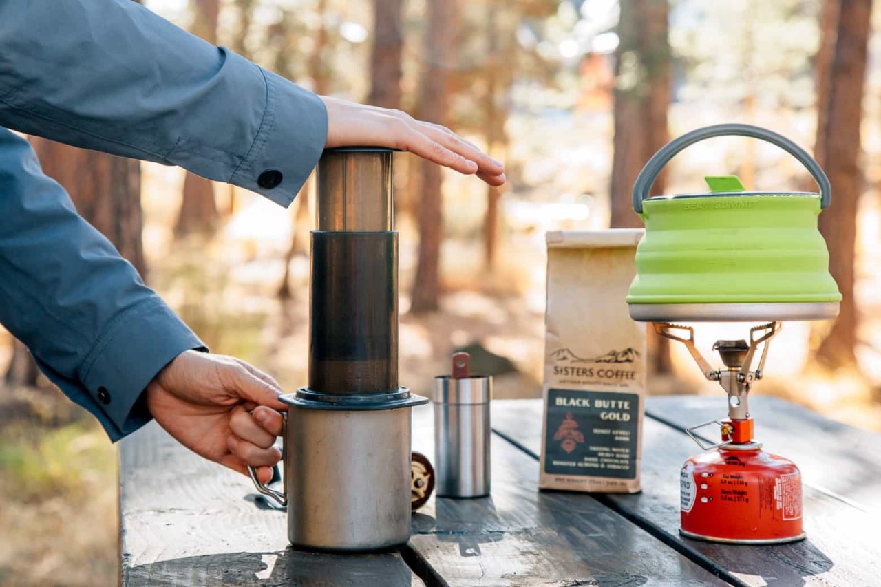 An AeroPress on a camping table with freshly ground coffee beside it